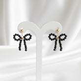 Black bow-shaped earrings on a white stand with a white background