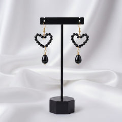 Heart-shaped earrings on a black stand against a white background