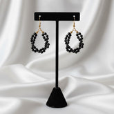 Black beaded earrings on a black stand against a white fabric background