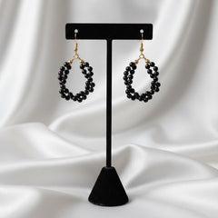Black beaded earrings on a black stand against a white fabric background