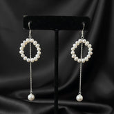 Pair of pearl earrings on a black stand against a black satin background