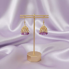 Gold earrings with purple gemstones on a gold stand against a purple satin background