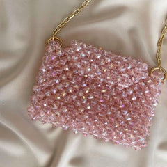 Pink beaded handbag with gold chain on a beige fabric background