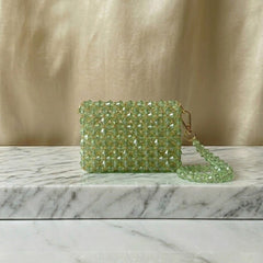 Green beaded clutch bag on a marble surface with a gold curtain background