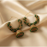 Gold and green hoop earrings on a beige fabric background