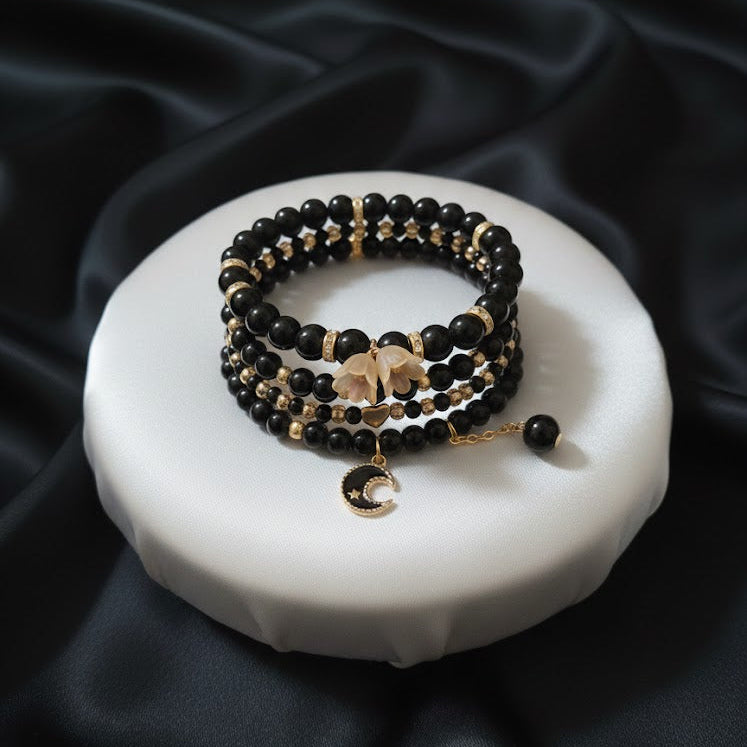 Black and gold beaded bracelets on a white ceramic dish with black satin background