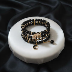 Black and gold beaded bracelets on a white ceramic dish with black satin background