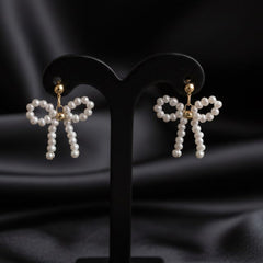 Pearl bow-shaped earrings on black stands against a dark fabric background