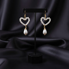 Heart-shaped pearl earrings on a black stand against a dark fabric background