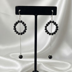 Black beaded earrings on a black earring stand against a white satin background