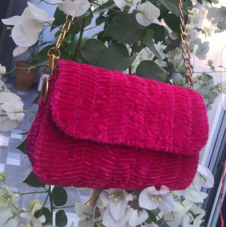 dark pink textured handbag hanging on a tree branch with white flowers in the background