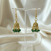 Gold earrings with green beads on a clear stand against a white satin background