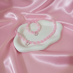 Pink necklace and bracelet set on a white heart-shaped pad with pink satin background