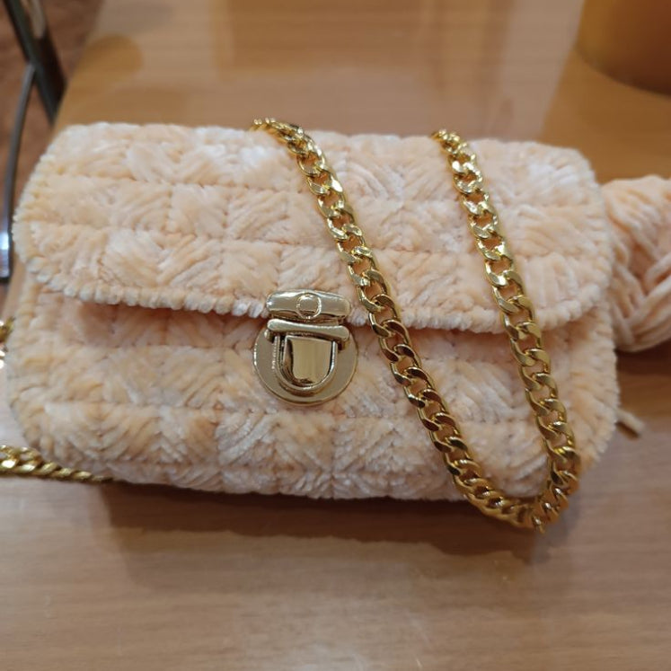 Beige textured handbag with a gold chain and clasp on a wooden surface.