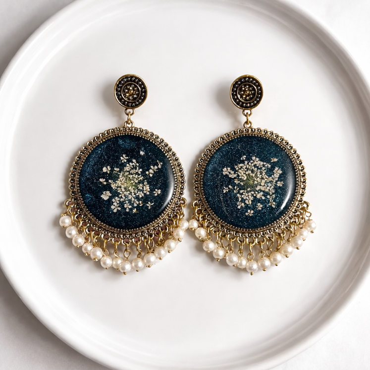 Pair of earrings with blue circular designs and pearl accents on a white plate.