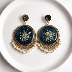 Pair of earrings with blue circular designs and pearl accents on a white plate.