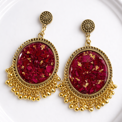 Gold-framed earrings with red central stones on a white plate