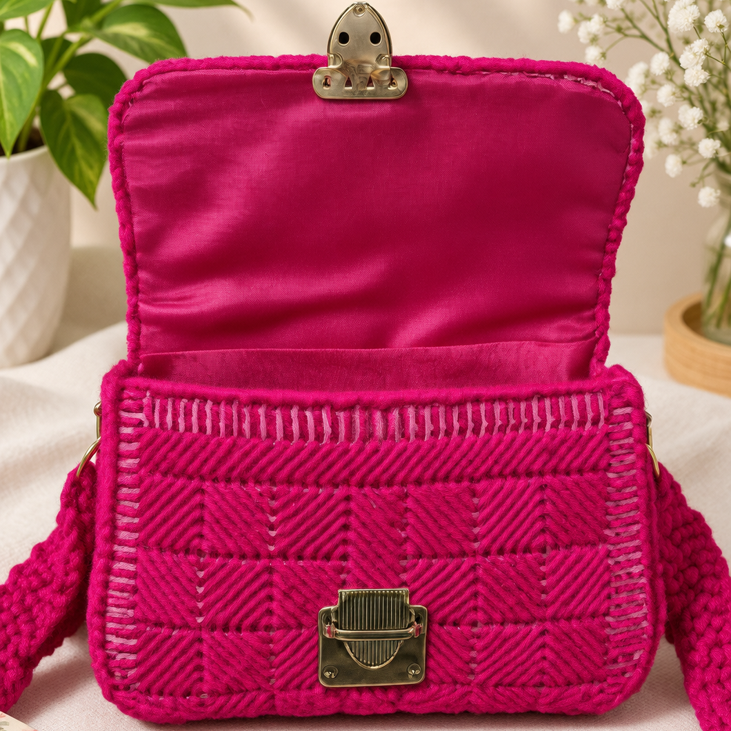 A bright fuchsia pink woven shoulder bag with a textured chevron pattern, featuring a satin-lined interior, a silver-tone top clasp, and a matching pink knotted strap, styled on a light fabric surface with decorative plants and a book.