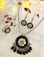 Jewelry set with daisy-themed pendant, earrings, and ring on a floral background