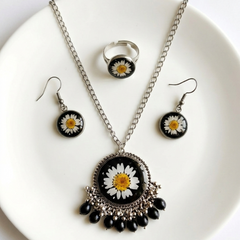 Jewelry set with necklace, earrings, and ring featuring daisy designs on a white plate.