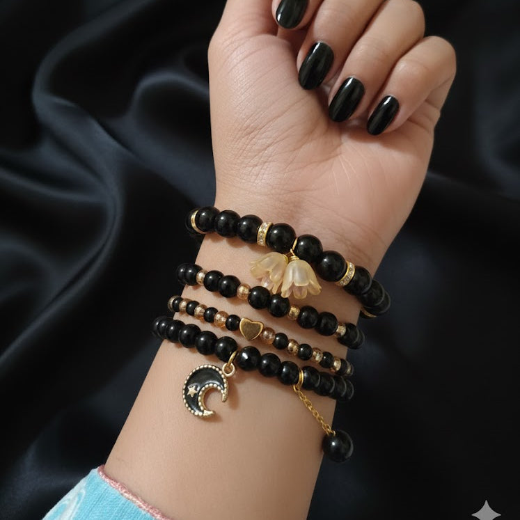 Hand wearing multiple black beaded bracelets with gold accents on a dark fabric background