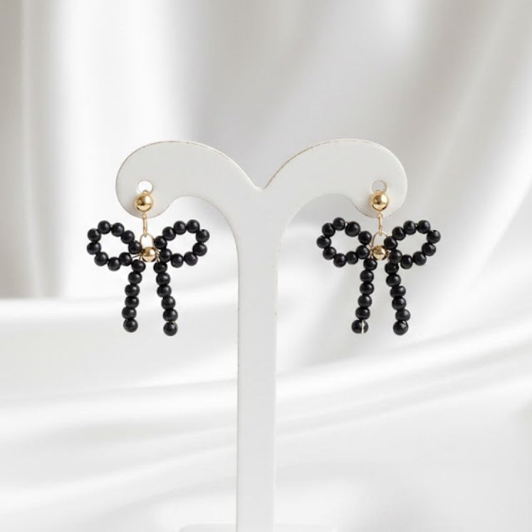 Black bow-shaped earrings on a white stand with a white background