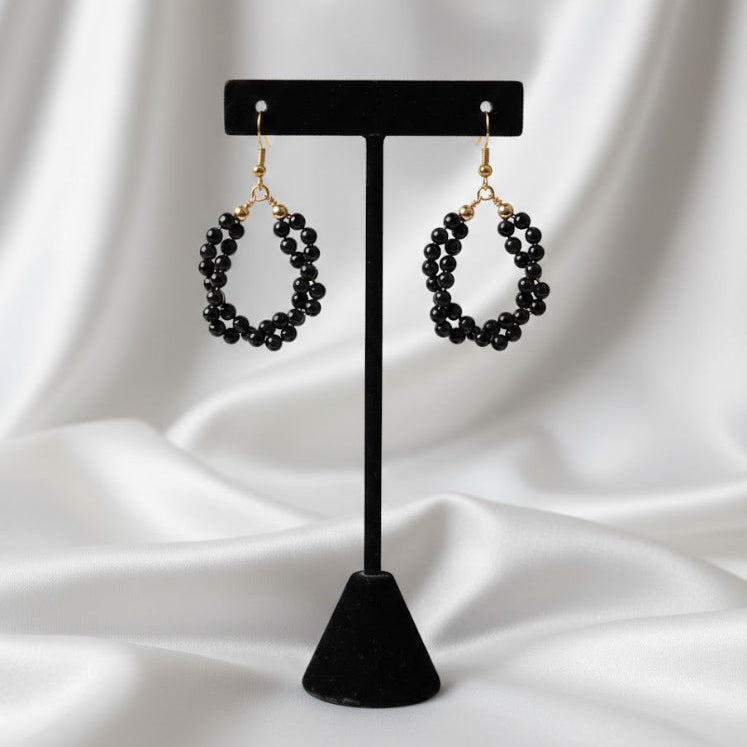 Black beaded earrings on a black stand against a white fabric background