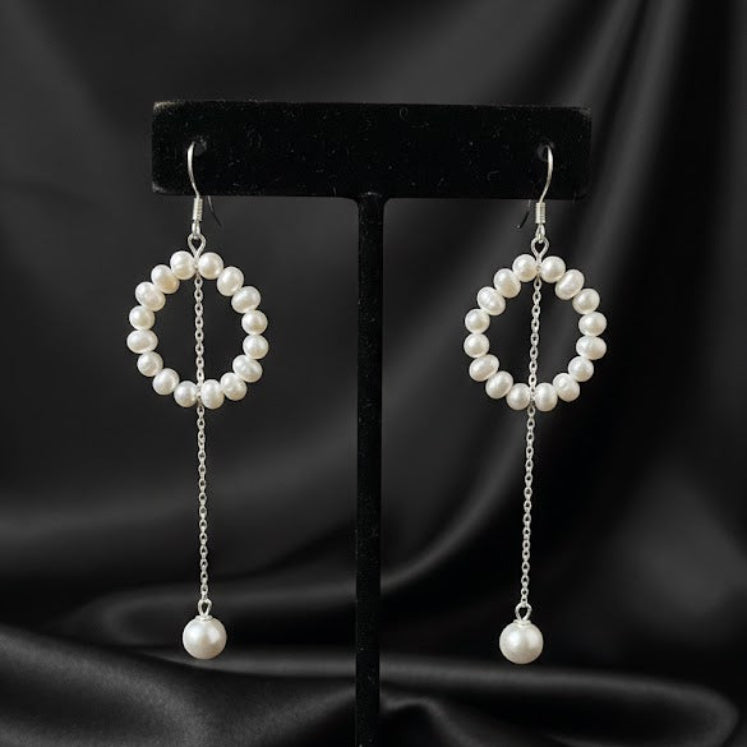 Pair of pearl earrings on a black stand against a black satin background