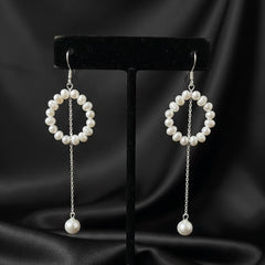 Pair of pearl earrings on a black stand against a black satin background