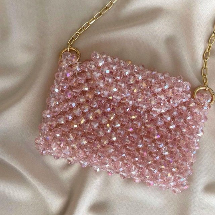 Pink beaded handbag with gold chain on a beige fabric background