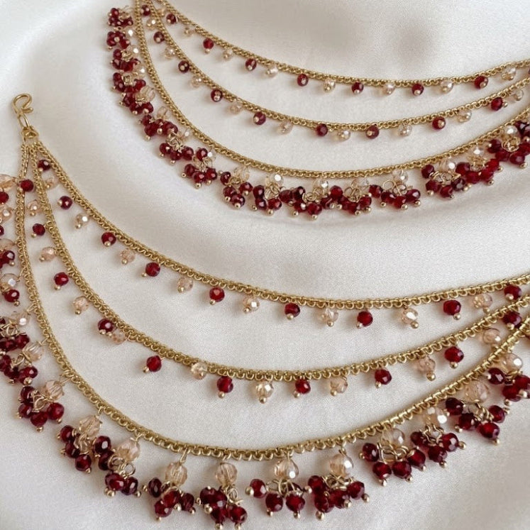 Three gold necklaces with red and clear beads on a white fabric background