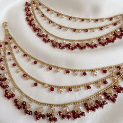 Three gold necklaces with red and clear beads on a white fabric background