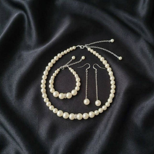 Pearl jewelry set including necklace, bracelet, and earrings on black satin fabric