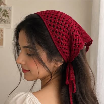 A woman wearing a deep red crocheted headscarf with tie details, shown in profile against a soft indoor background.