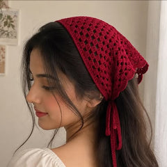 A woman wearing a deep red crocheted headscarf with tie details, shown in profile against a soft indoor background.