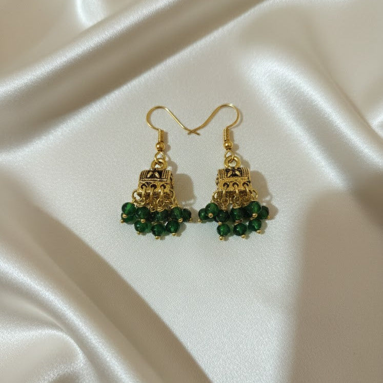 Gold earrings with green beads on a satin surface