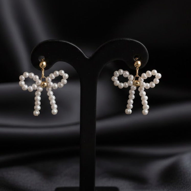 Pearl bow-shaped earrings on black stands against a dark fabric background