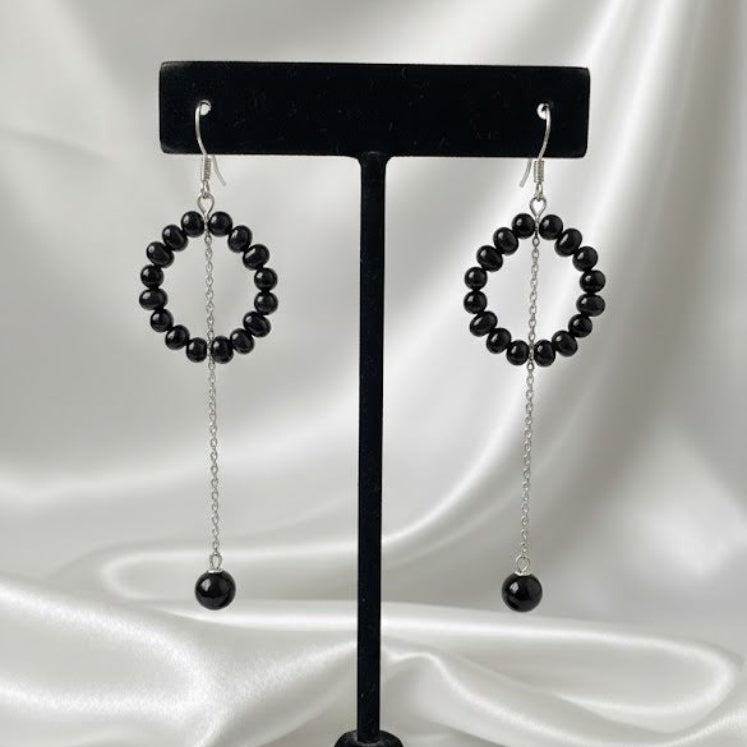 Black beaded earrings on a black earring stand against a white satin background