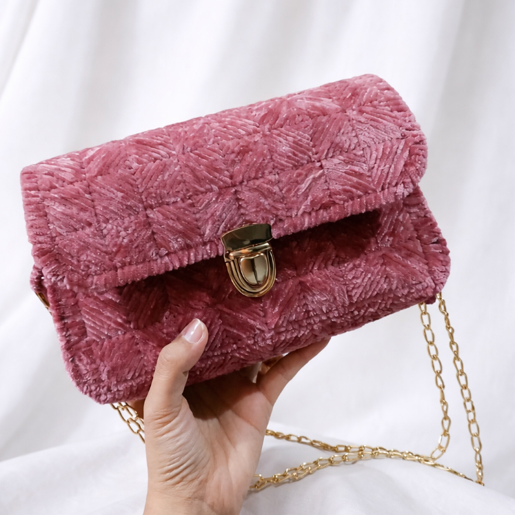Pink textured handbag with a gold chain held by a hand against a white background