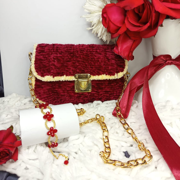 Red textured handbag with gold chain on a white surface with red flowers.