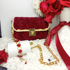 Red textured handbag with gold chain on a white surface with red flowers.