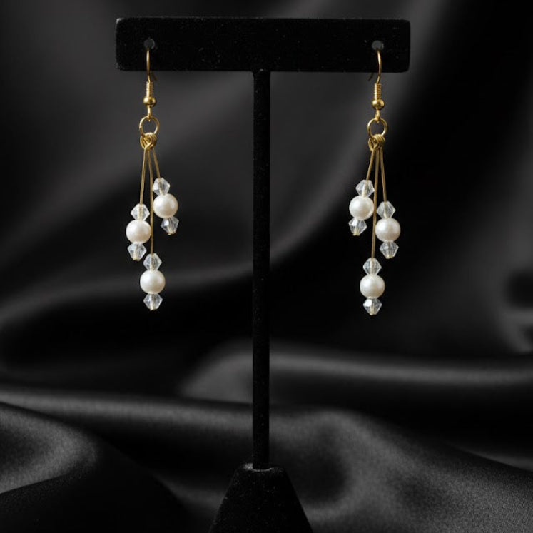 Pair of pearl earrings on a black stand against a black satin background