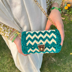 Person holding a teal and white zigzag patterned handbag with a gold chain strap.