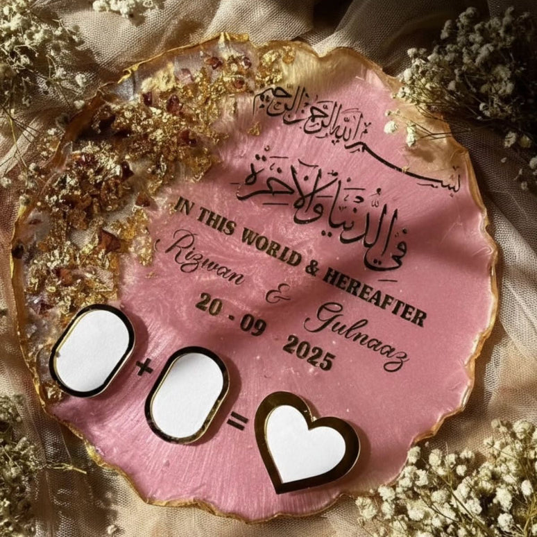 Personalized pink plaque with Arabic text and dates, surrounded by flowers on a soft fabric background.