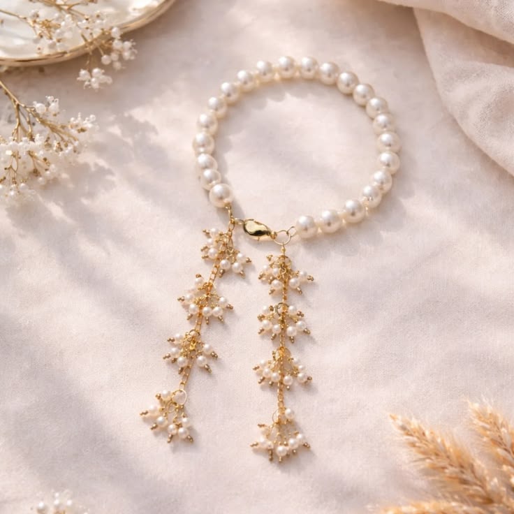 Pearl bracelet with gold floral pendants on a soft fabric background