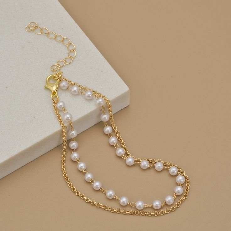 Gold chain bracelet with pearls on a beige surface